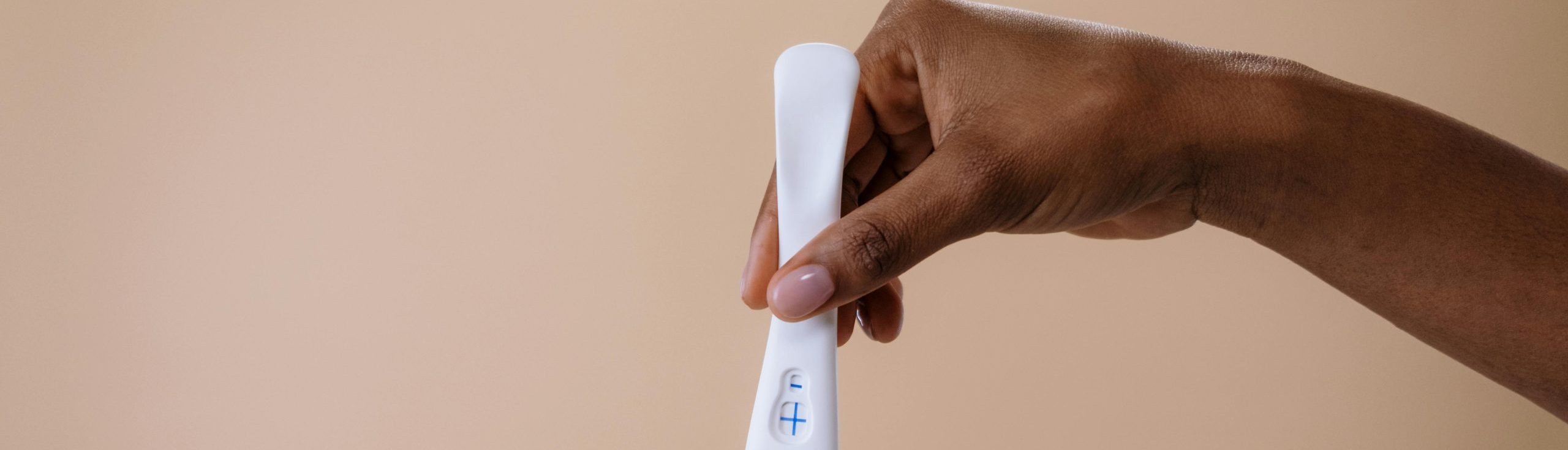 Positive pregnancy test being held by a hand against a brown background